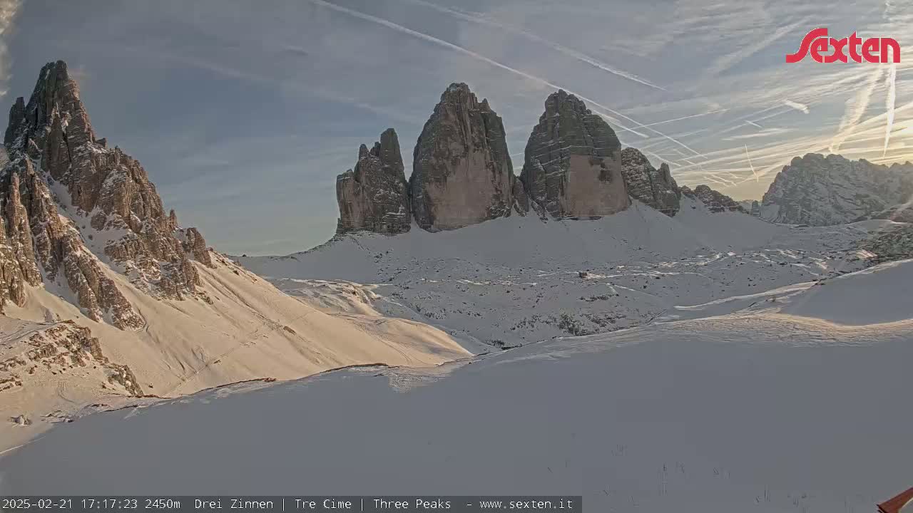 A snow-covered mountain range with several prominent peaks is visible under a mostly clear sky with contrails.