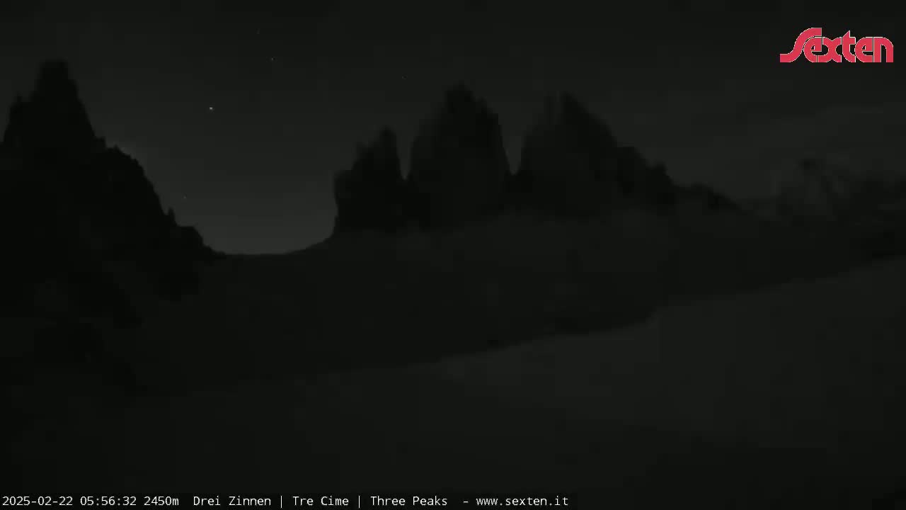 A nighttime, low-light image shows a dark, mountainous landscape under a mostly clear sky with a few visible stars.