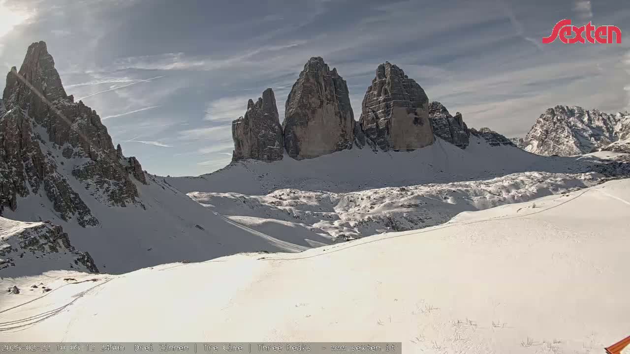 A snow-covered mountain range with several prominent peaks is visible under a partly sunny sky.