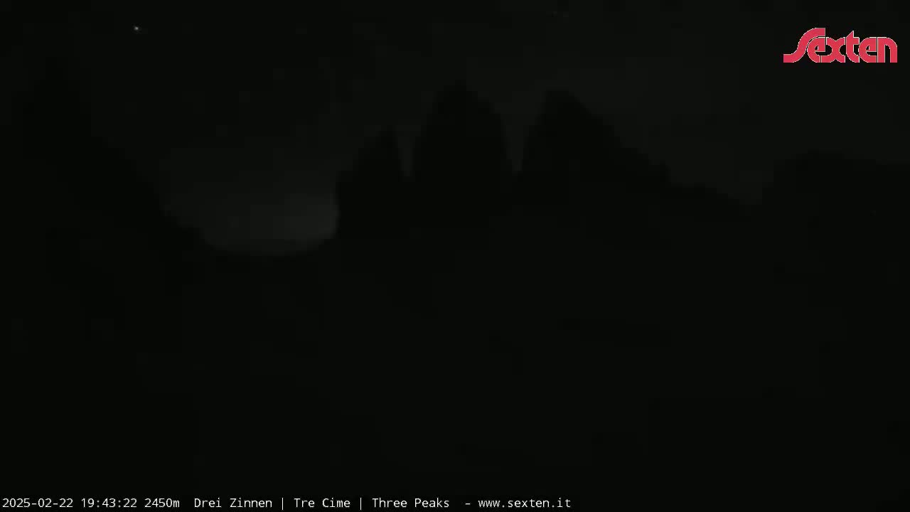 A dark, nighttime scene shows indistinct, silhouetted shapes that appear to be trees or hills under a mostly clear sky.