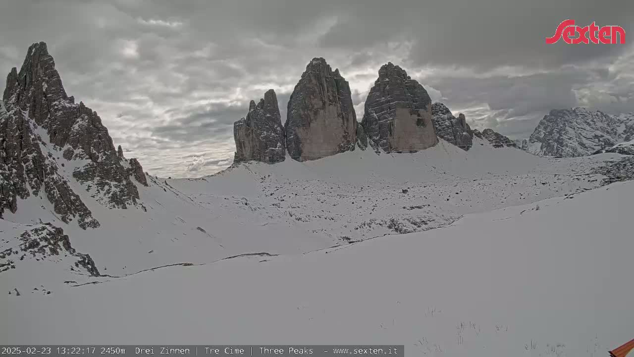 A snow-covered mountain valley with several prominent rock formations under a cloudy sky.