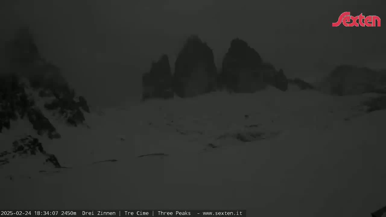A snow-covered landscape with dark, indistinct mountain peaks in the distance under foggy conditions.