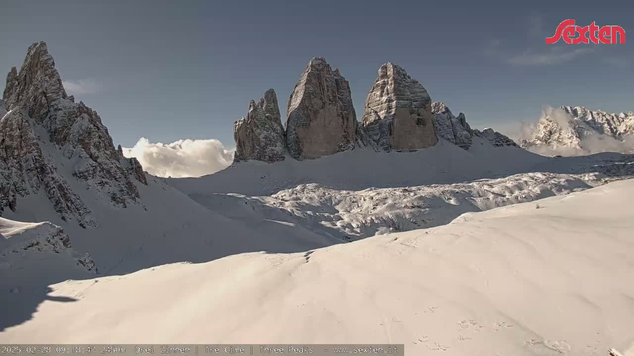 A snow-covered mountain range with several prominent peaks is visible under a mostly clear sky with some clouds.