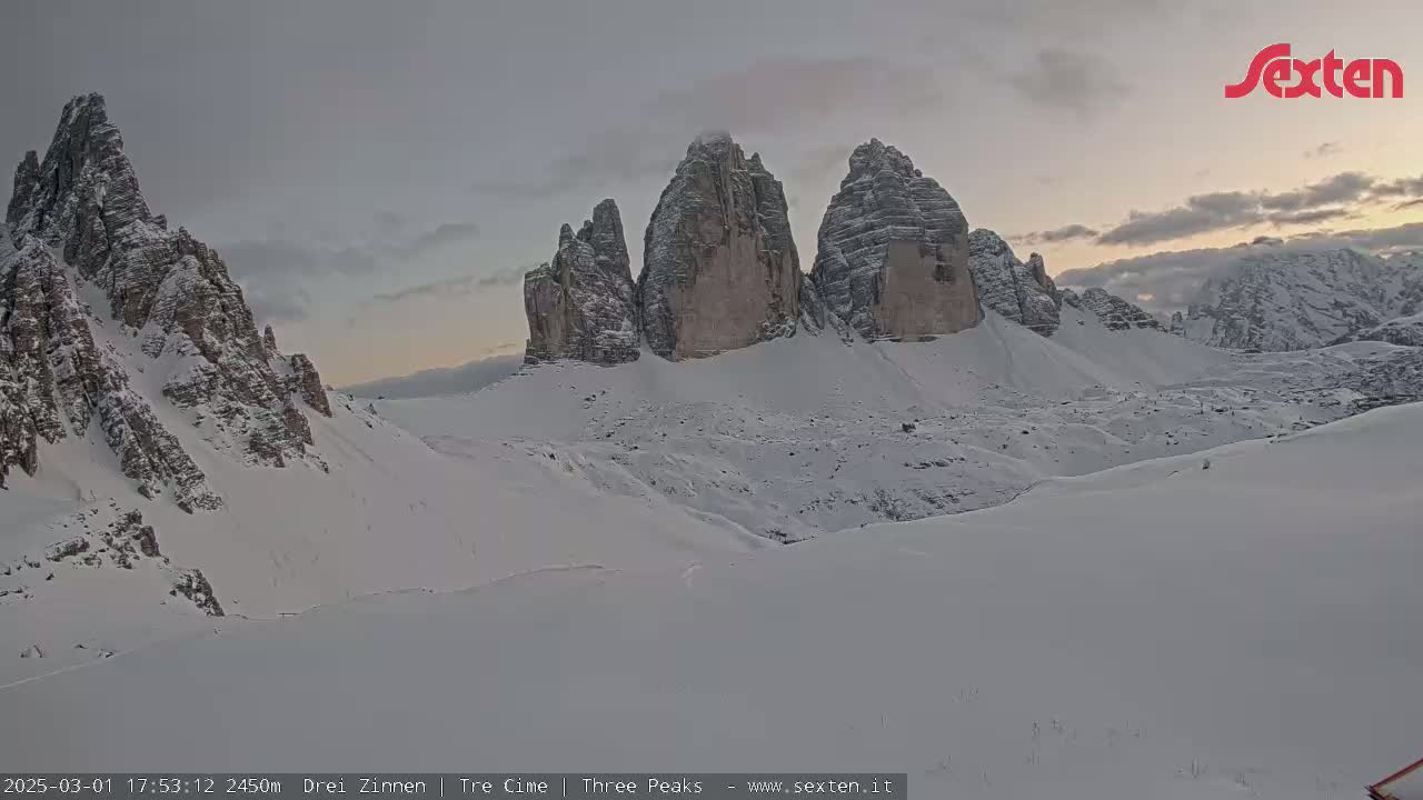 A snow-covered mountain landscape shows several large, jagged peaks under a twilight sky.