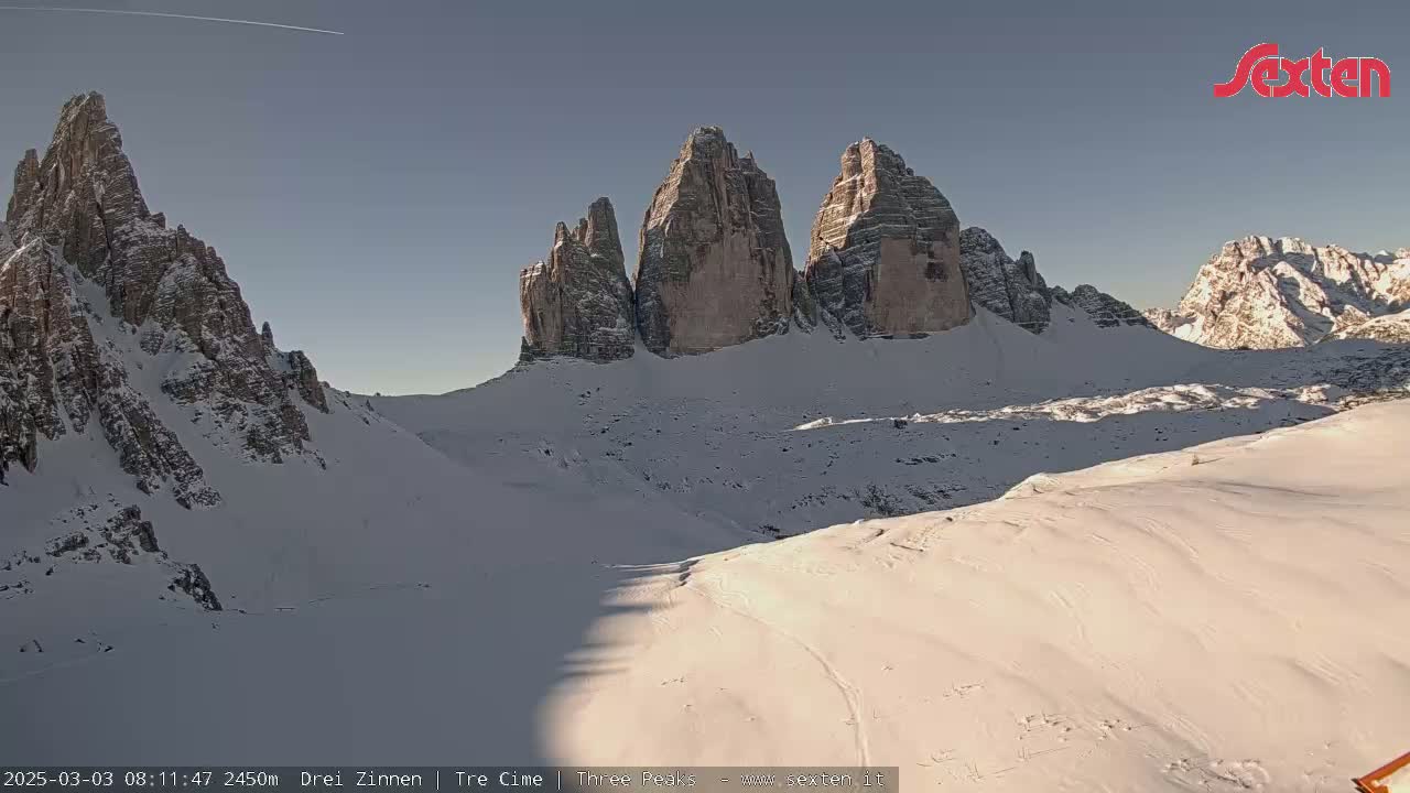 A snow-covered mountain range with several prominent, rocky peaks under a clear, bright sky.
