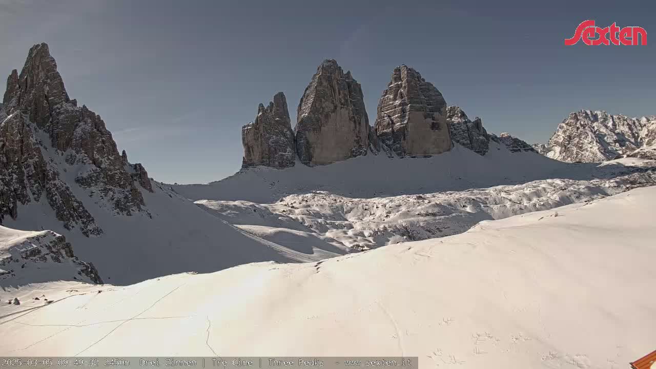 A snow-covered mountain range with prominent, tall rock formations under a clear sky.