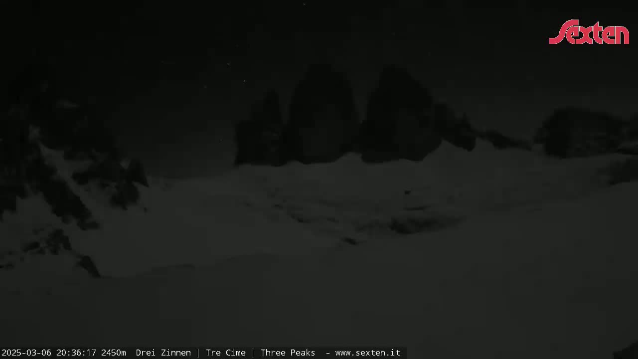 A nighttime, snowy scene shows three dark, snow-covered peaks under a dark sky.