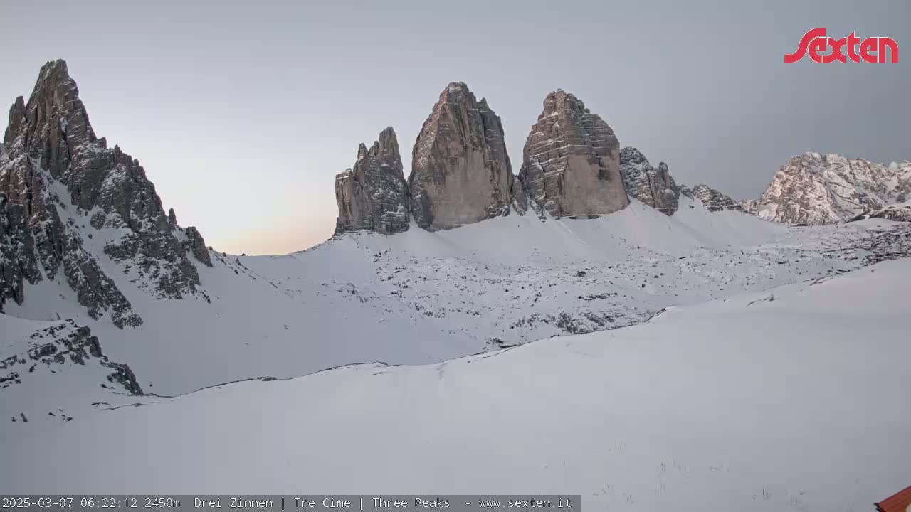 A snow-covered mountain range with prominent, jagged peaks is visible under a pale sky at dawn.