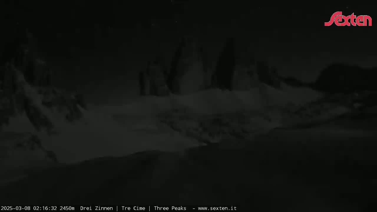 A nighttime, low-light image shows a snow-covered mountain range under a dark sky.