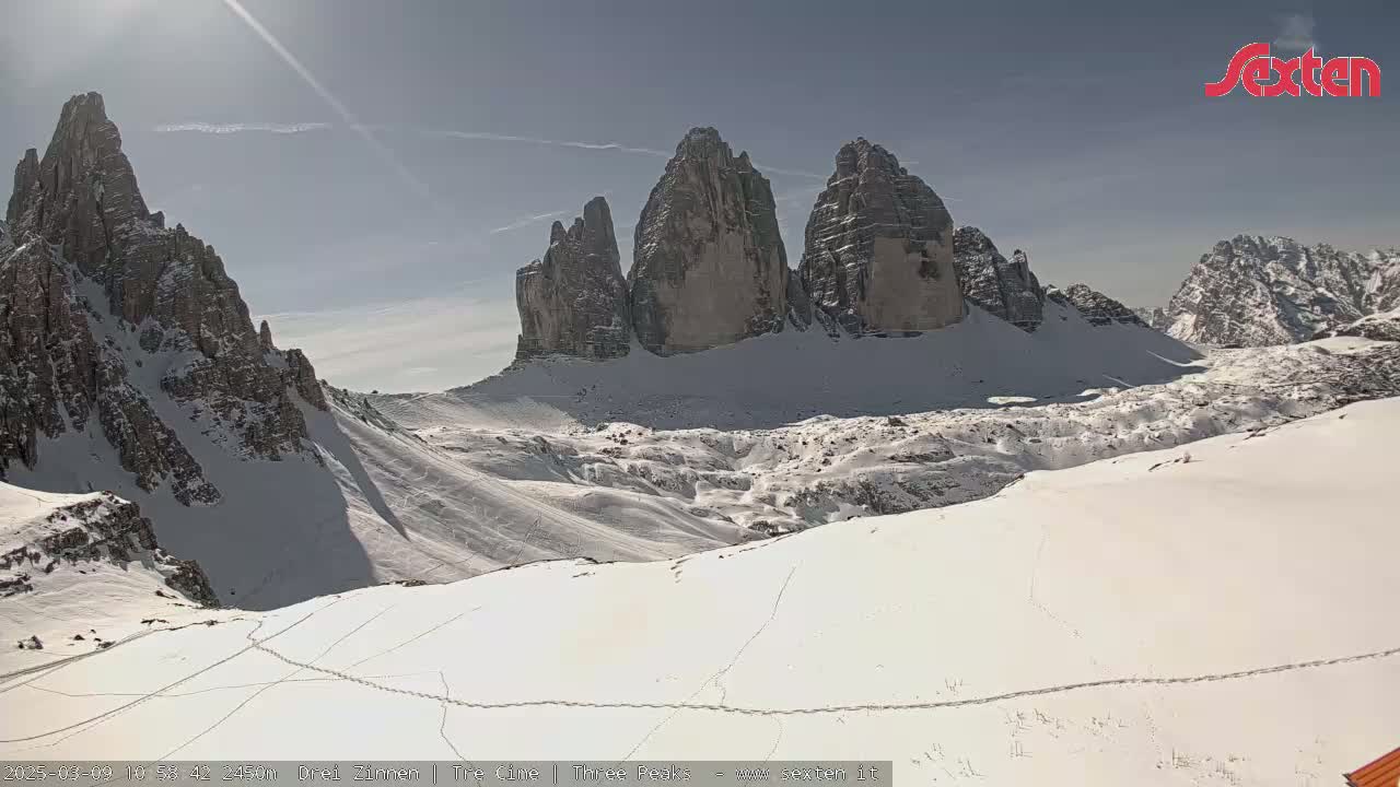 A snow-covered mountain range with several prominent peaks is visible under a mostly sunny sky.