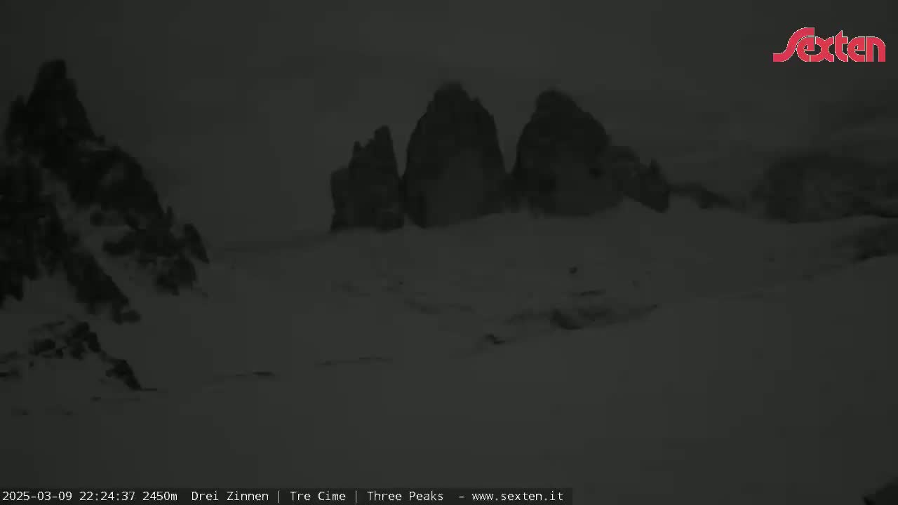 A dark, snowy landscape features three prominent rock formations in the distance under an overcast sky.