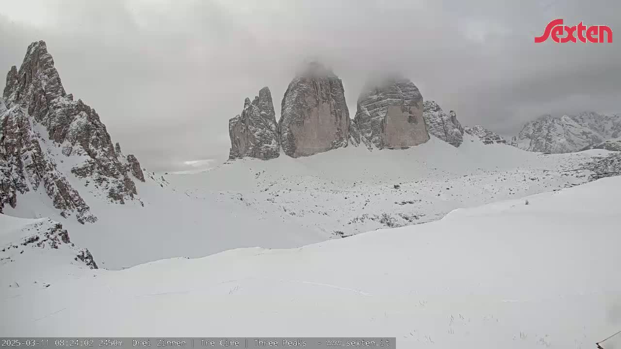 Snow-covered mountains, including three prominent peaks partially obscured by fog, are visible under an overcast sky.