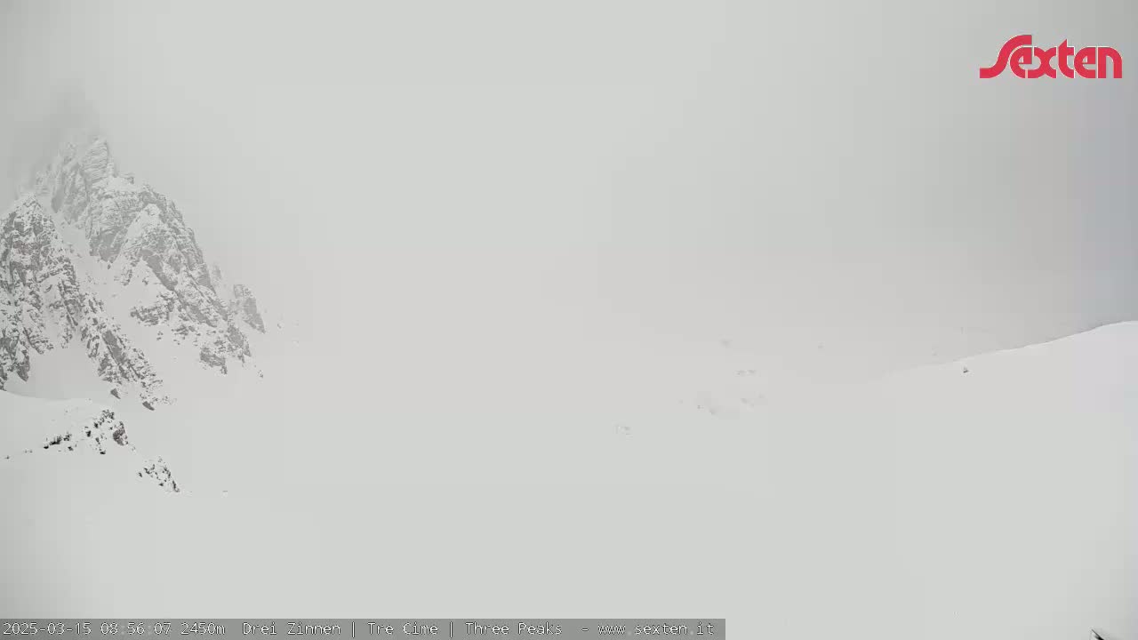 A snow-covered mountain peak is partially obscured by heavy fog or snow in a mountainous landscape.
