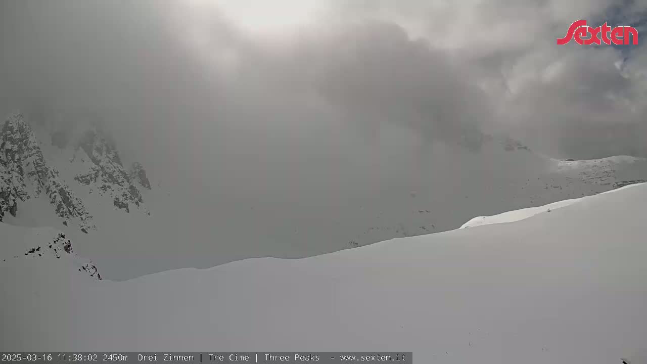 A snow-covered mountain range is mostly obscured by heavy fog under an overcast sky.
