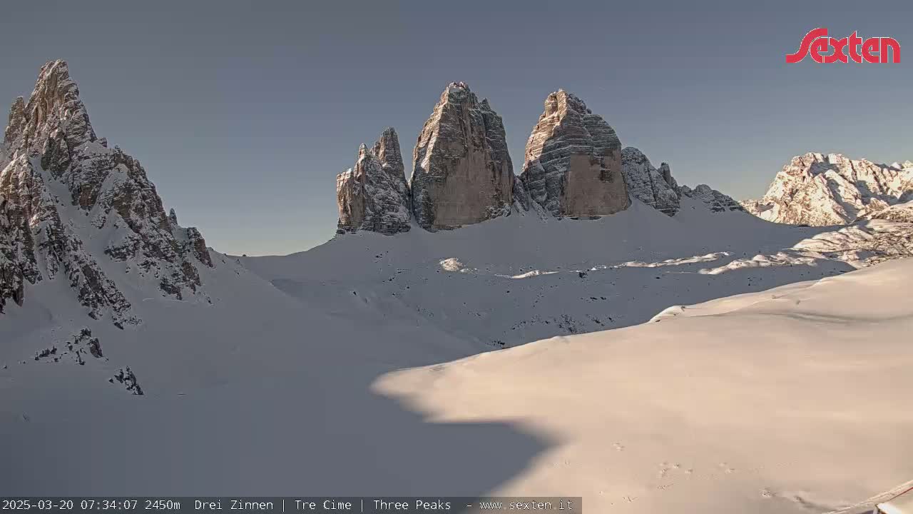 A snow-covered mountain range with prominent rock formations is visible under a clear, bright sky.