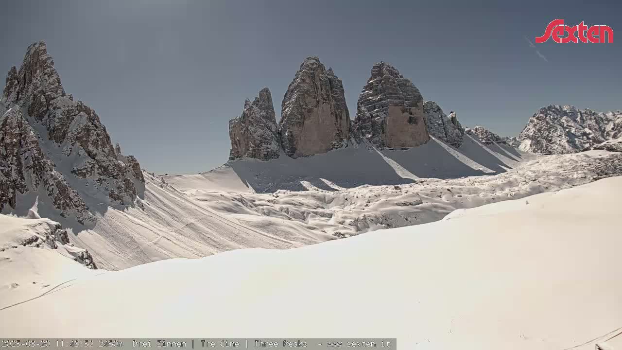A snow-covered mountain valley with three prominent rock formations, under a mostly sunny sky.