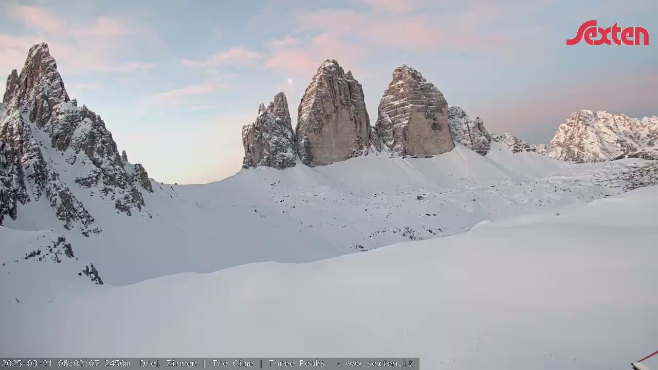 A snow-covered mountain range with prominent rock formations is visible under a pale, dusky sky.