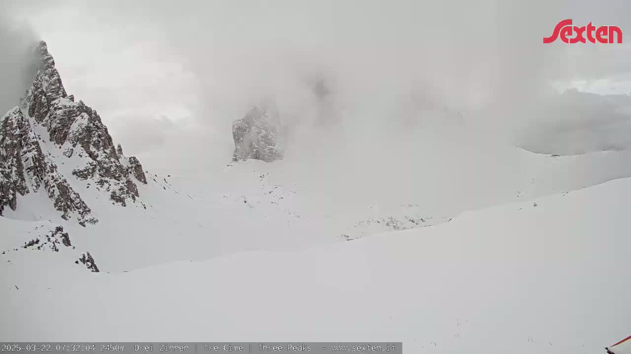 A snow-covered mountainous landscape is shrouded in fog.