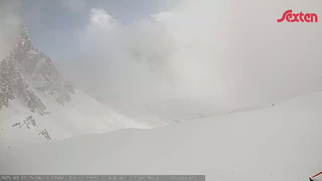 A snow-covered mountain peak is partially obscured by fog or blowing snow.