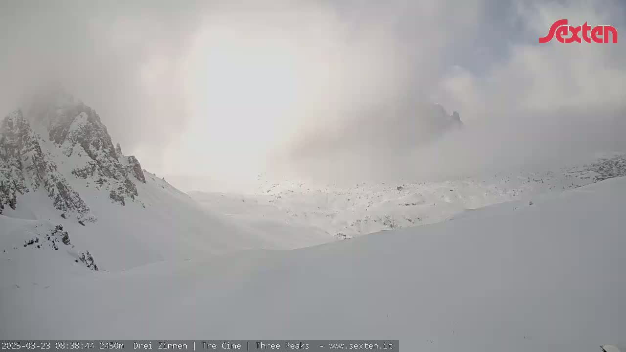 A snow-covered mountainous landscape is shrouded in fog and low clouds on an overcast day.