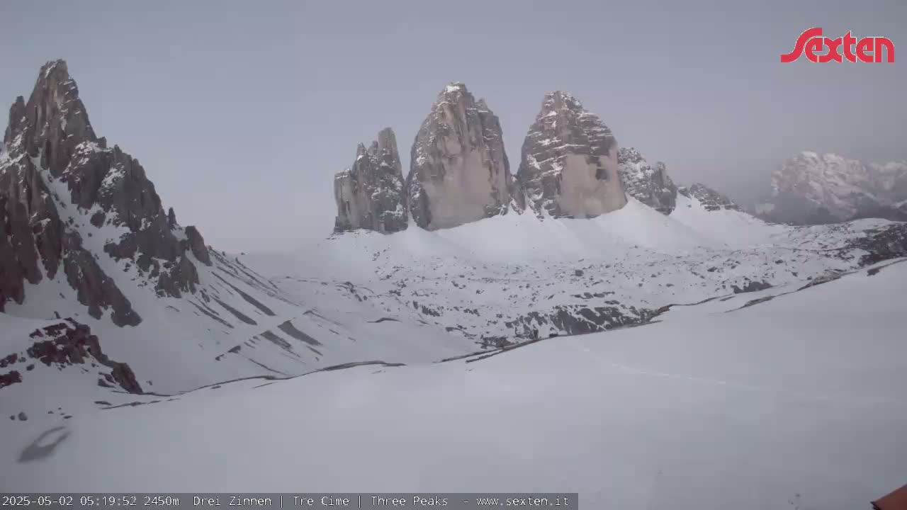 A snow-covered mountain range, including three prominent peaks, is visible under an overcast sky.