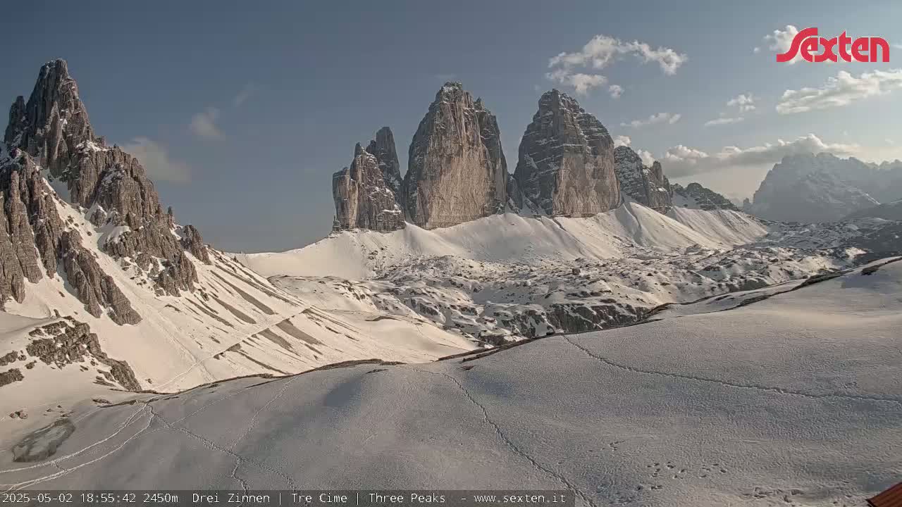 A snow-covered mountain landscape displays several jagged peaks under a mostly clear sky.