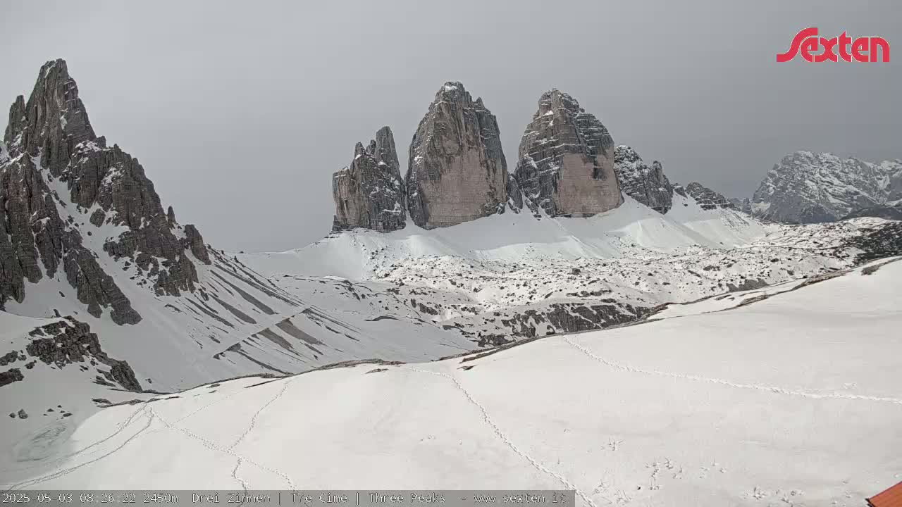 A snow-covered mountain range with three prominent peaks is visible under an overcast sky.