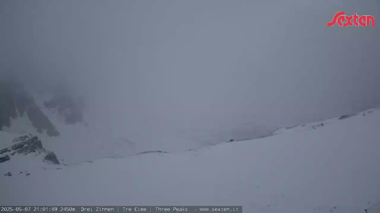 A snow-covered mountain landscape is shrouded in heavy fog.