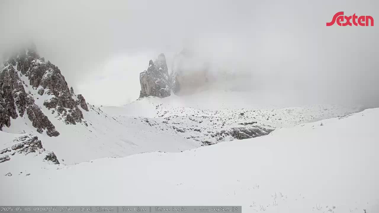 Snow-covered rocky mountains are partially obscured by fog.