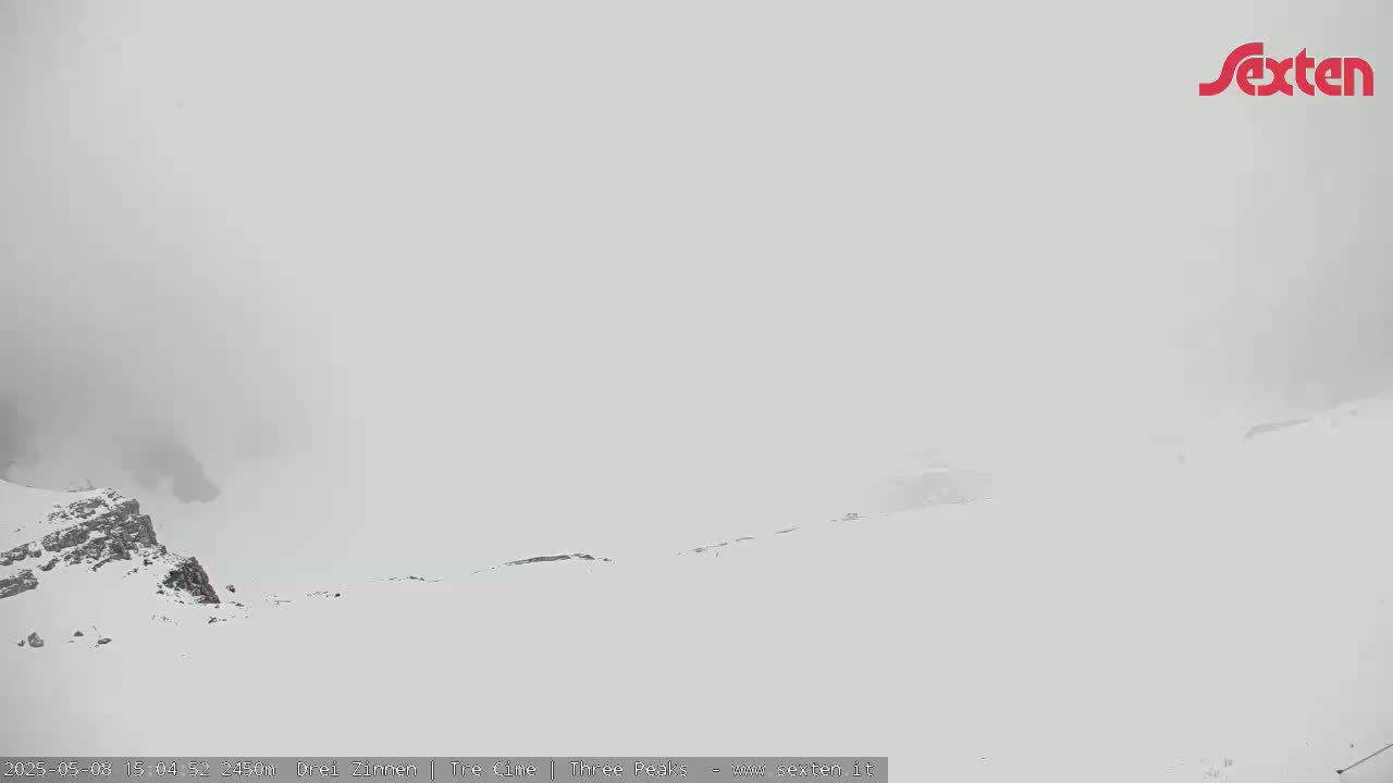A snow-covered mountain landscape is shrouded in thick fog.