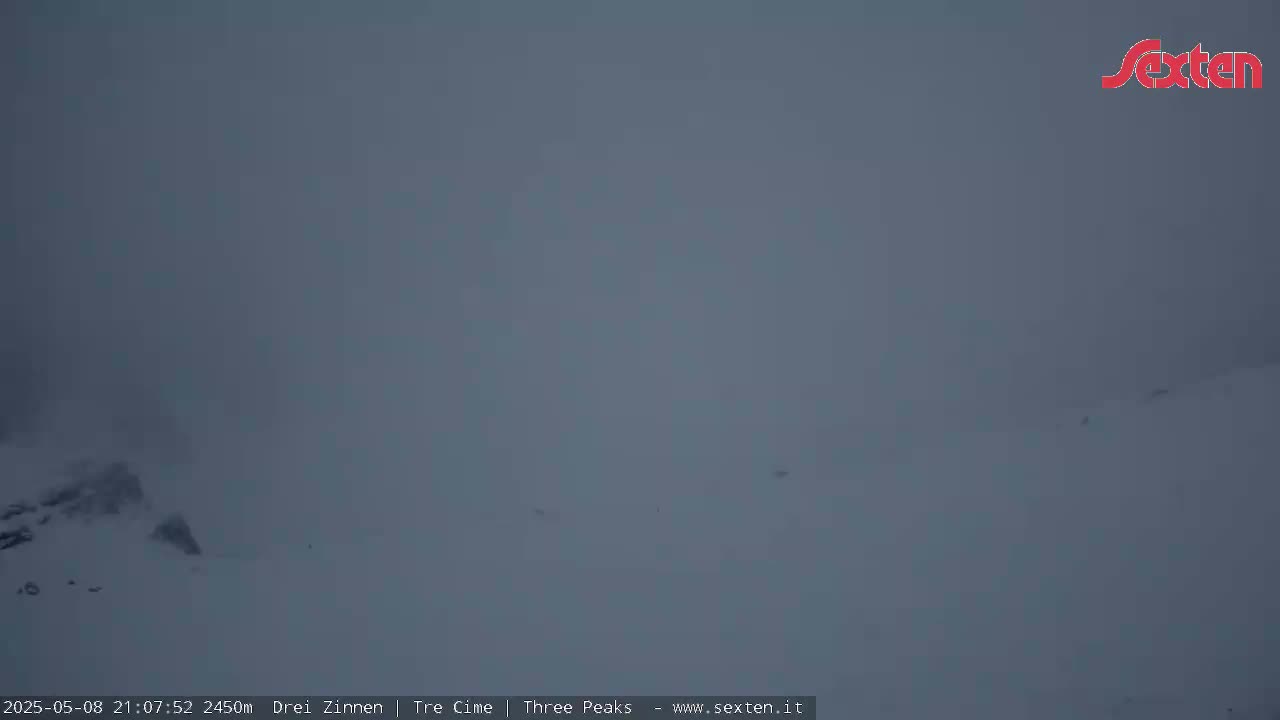 A snow-covered landscape is shrouded in heavy fog or low-lying clouds.