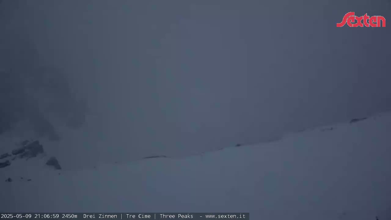 A snow-covered landscape is obscured by heavy fog or low clouds.