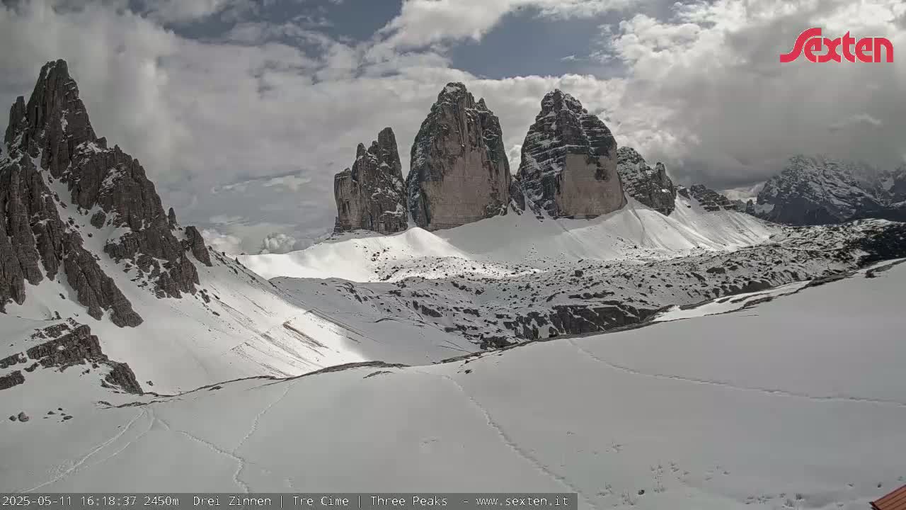 A snow-covered mountain range with prominent rock formations is visible under a partly cloudy sky.