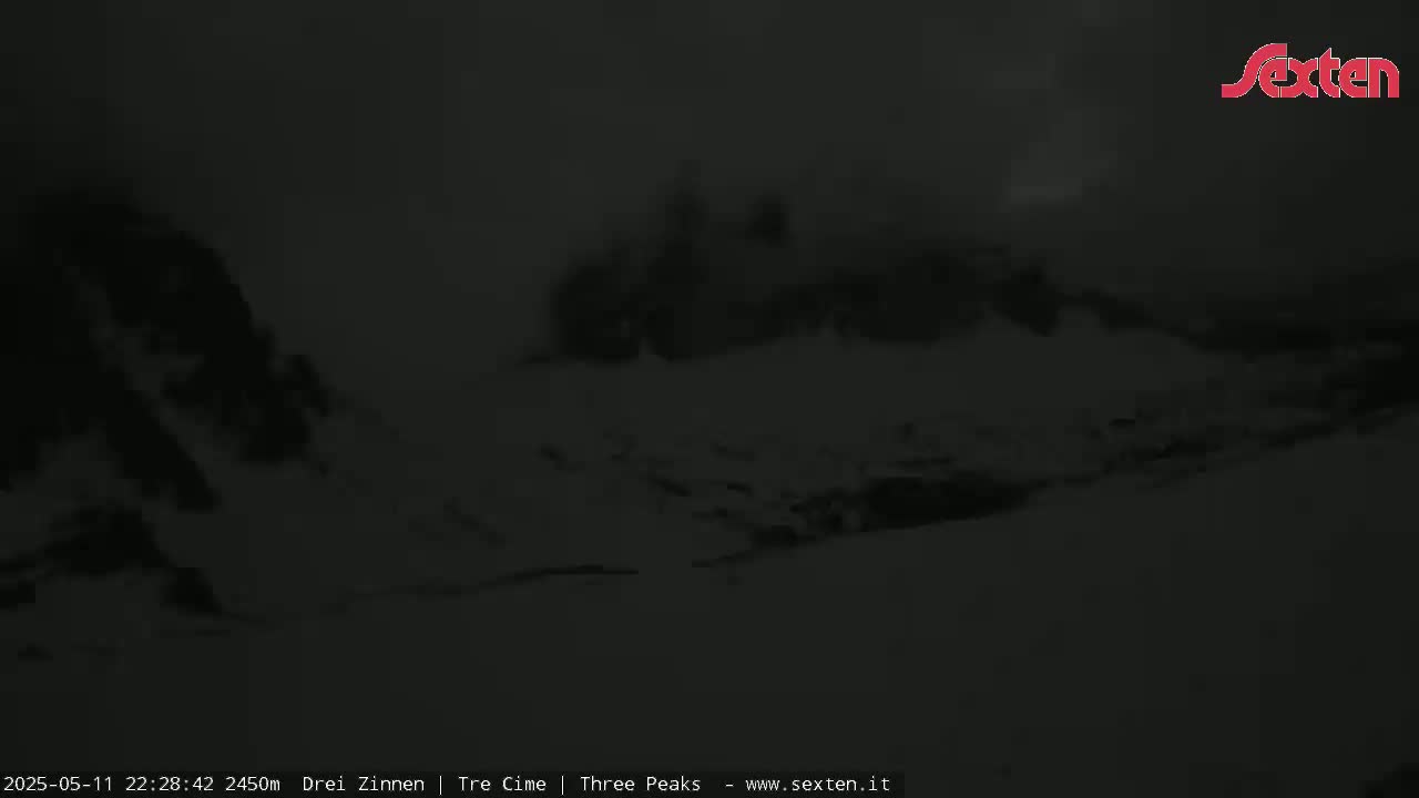 A nighttime, snow-covered mountain range is visible under a dark, cloudy sky.