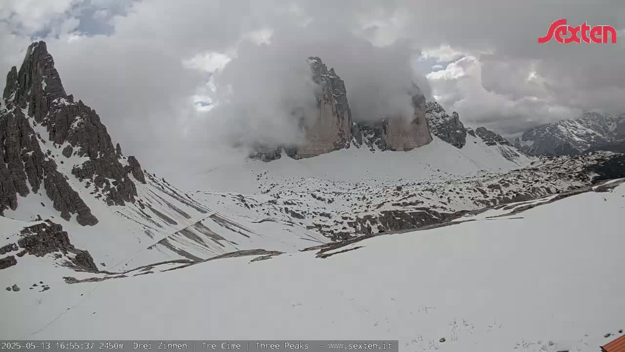 A snow-covered mountain range with rocky peaks partially obscured by clouds is visible on an overcast day.