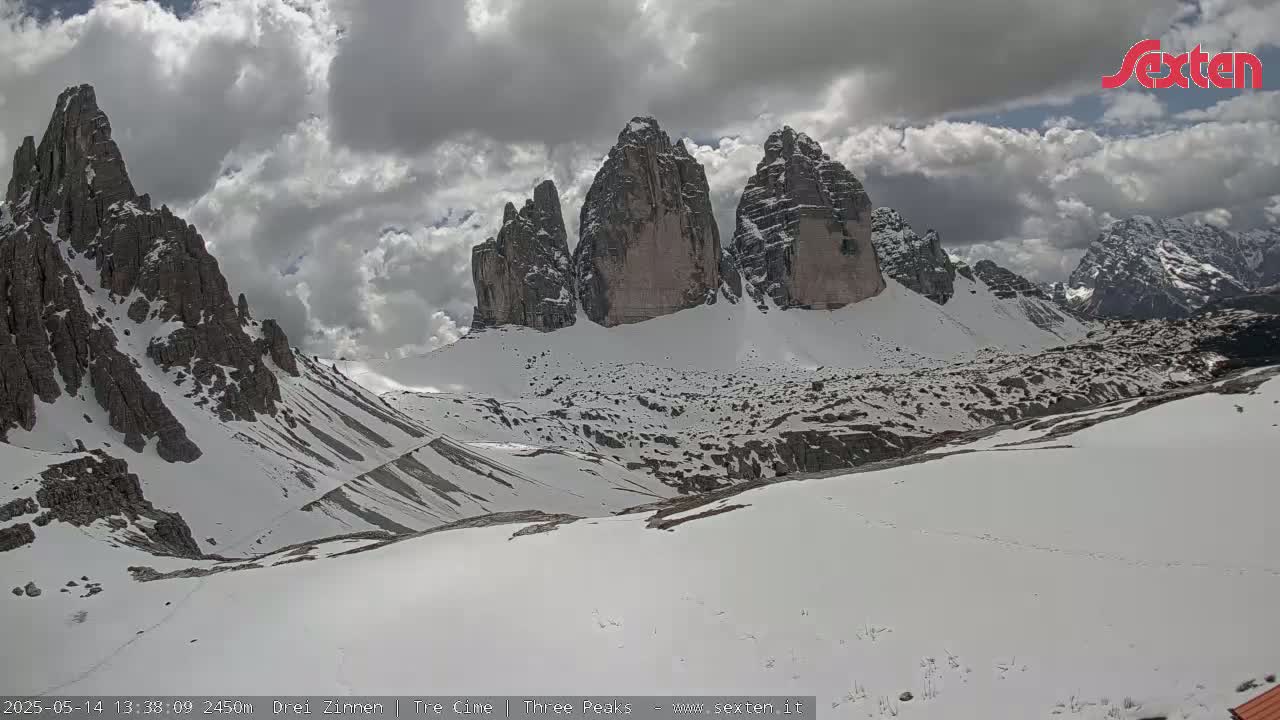 A snow-covered mountain valley with several jagged peaks under a partly cloudy sky.