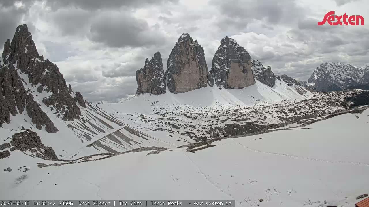 A snow-covered mountain range with several prominent, steep peaks is visible under a cloudy sky.