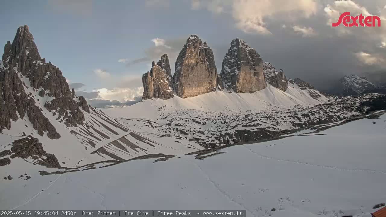 Snow-covered mountains, including three prominent peaks, are visible under a partly cloudy sky.