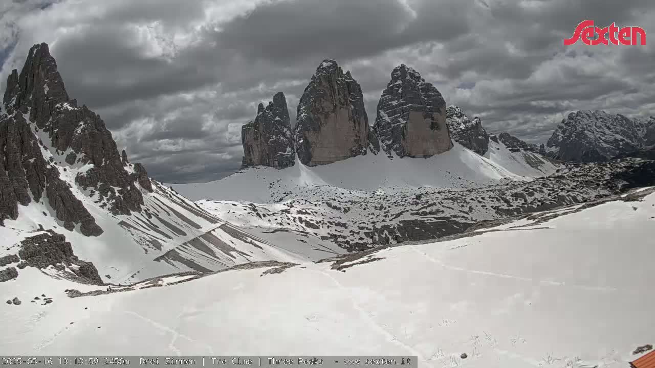 A snow-covered mountain range with prominent, tall rock formations under a cloudy sky.