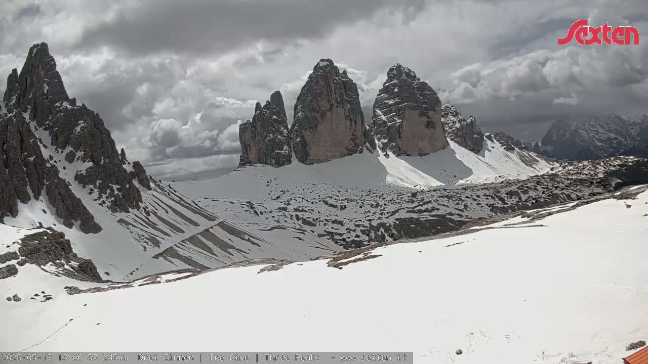 A snow-covered mountain valley with several jagged peaks under a cloudy sky.