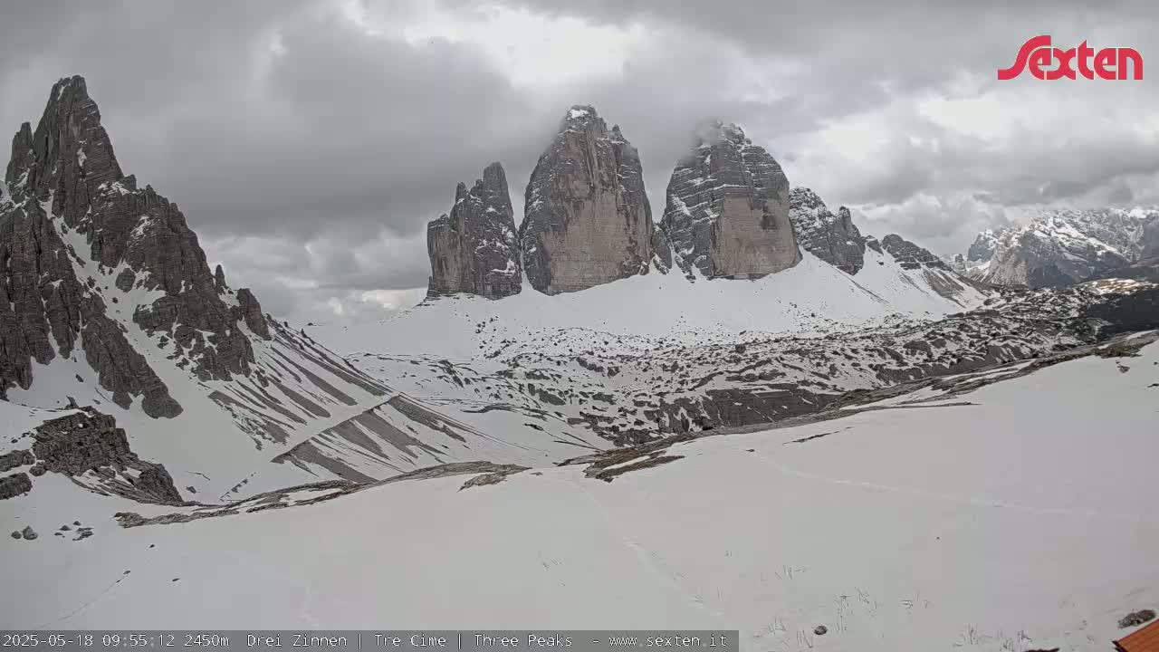 A snow-covered mountain landscape with three prominent peaks under an overcast sky.