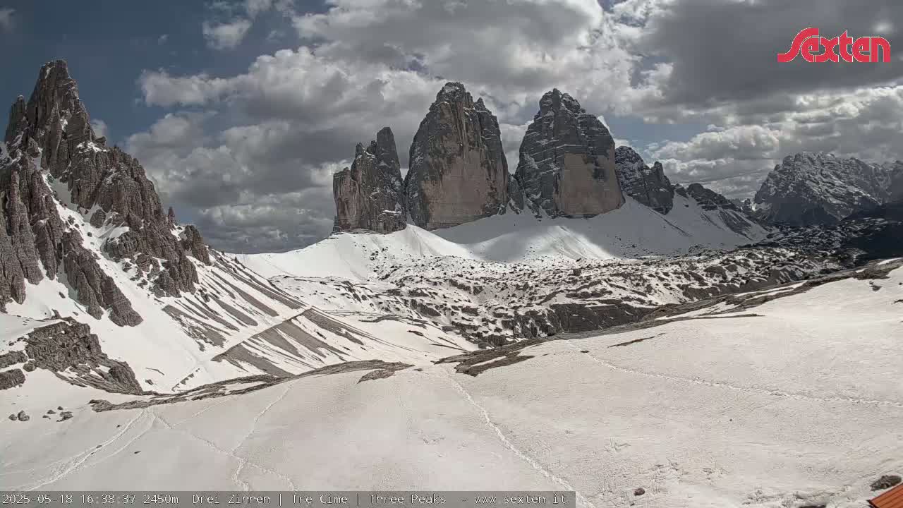 A snow-covered mountain valley with several prominent rock formations under a partly cloudy sky.