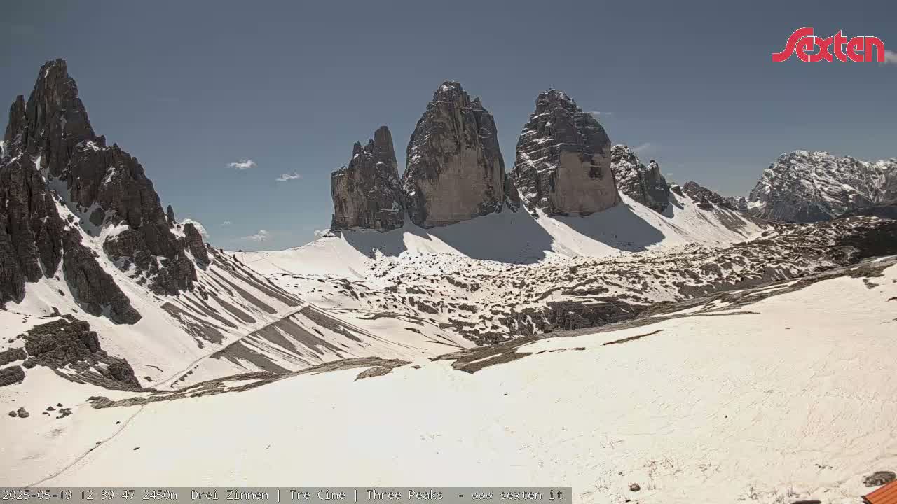 A snow-dusted mountain valley with several prominent rock formations under a mostly clear sky.