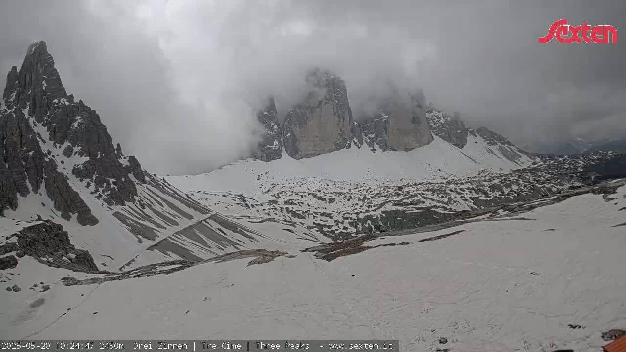 A snow-covered mountain valley is partially obscured by a cloudy, overcast sky.