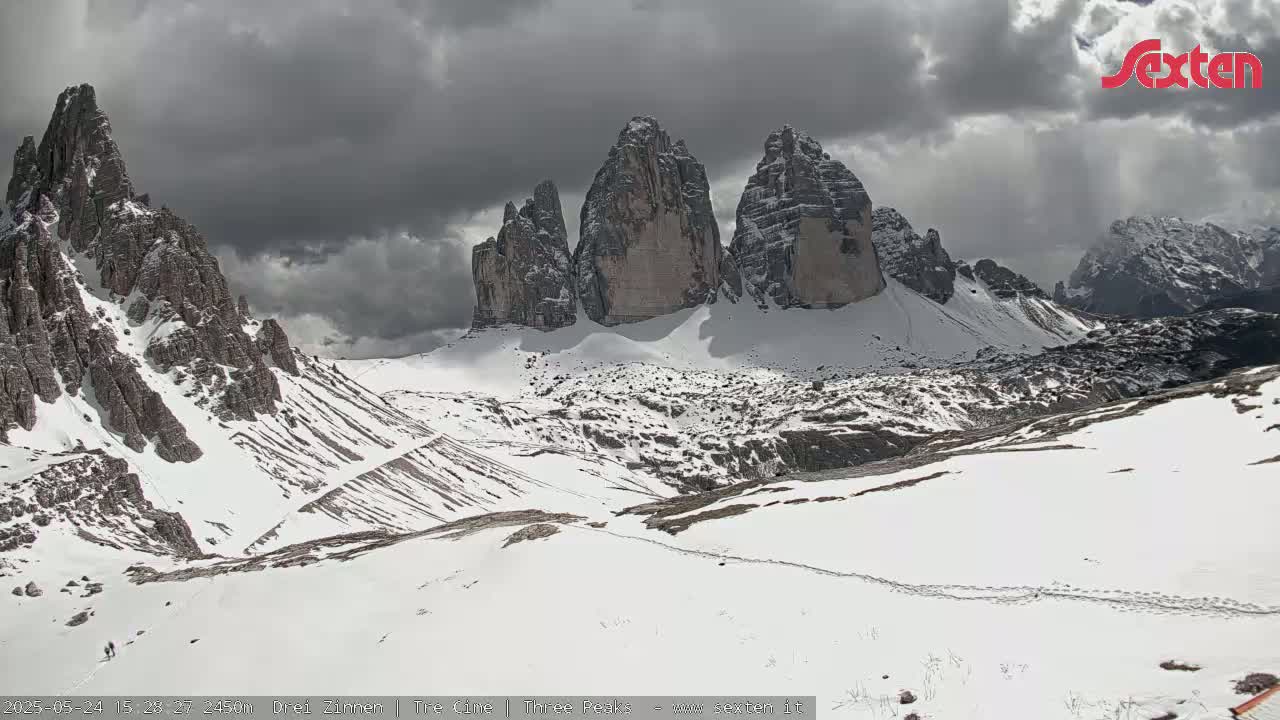 A snow-covered mountain range with several prominent peaks is visible under a cloudy sky.
