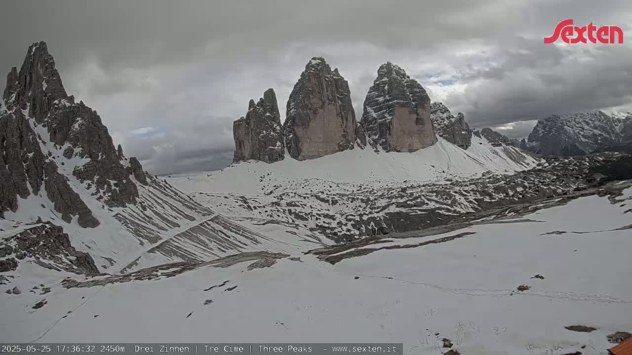 A snow-covered mountain landscape with several prominent rock formations under an overcast sky.