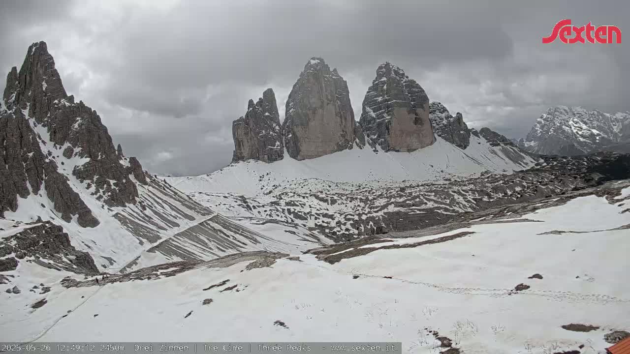 A snow-covered mountain range with prominent, tall rock formations is visible under an overcast sky.