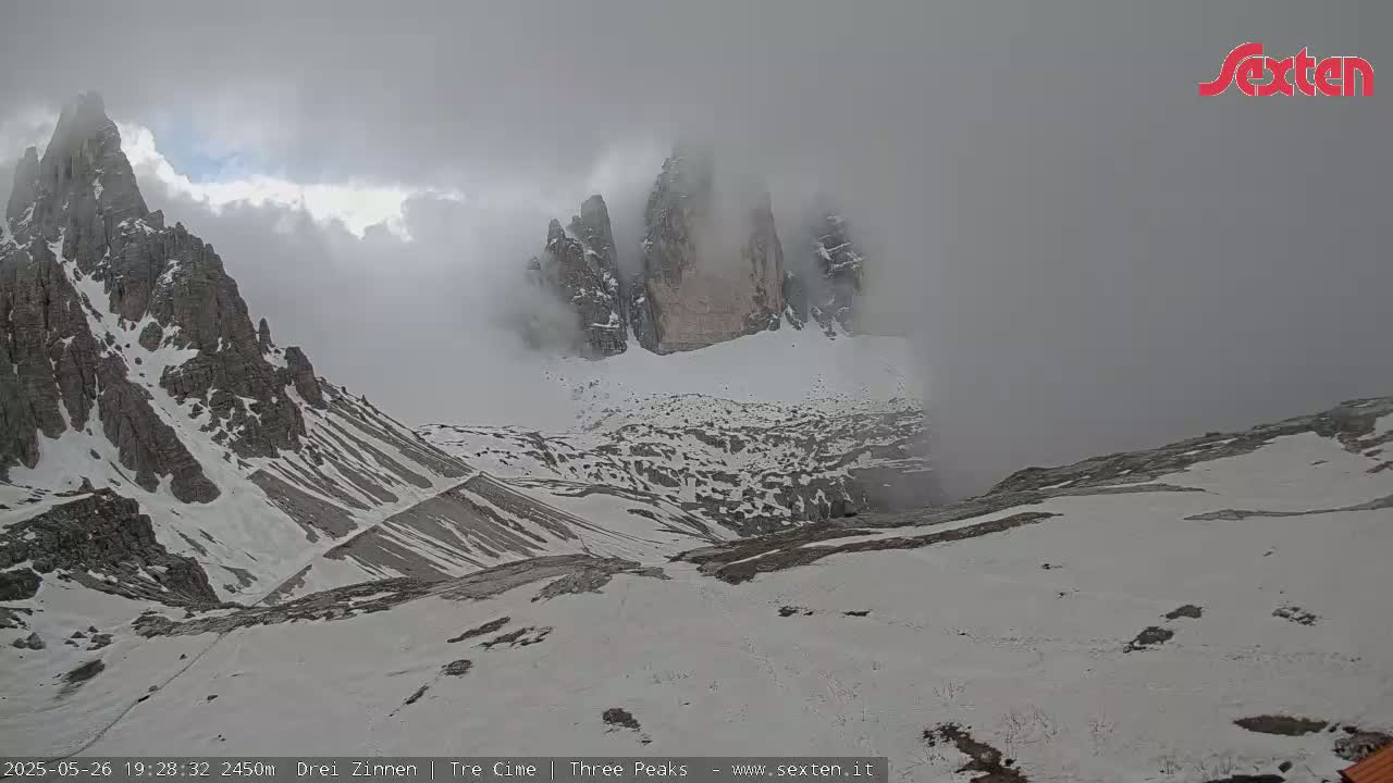A snow-covered mountain range is partially obscured by fog, with rocky peaks visible through the clouds.