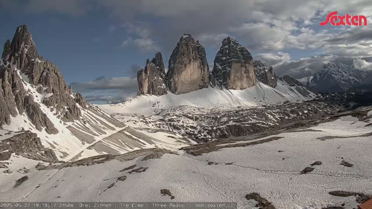 A snow-covered mountain range with several prominent peaks is visible under a partly cloudy sky.