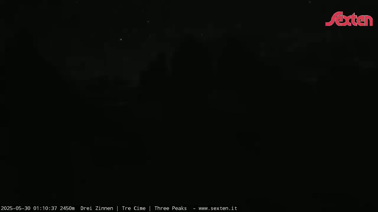 The image shows a dark, nighttime scene with a few faint lights visible in the distance under a clear sky.